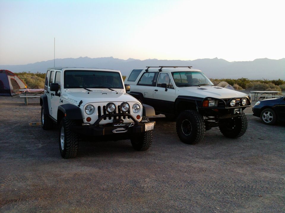 White Toyota 4Runner with black fender flares and roof rack, lifted with large tires, parked on dirt