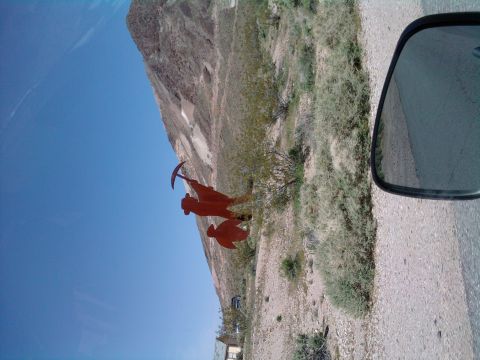 1985 Toyota 4Runner - A roadside sculpture of a miner and a bird stands against a desert mountain backdrop, viewed from a car.