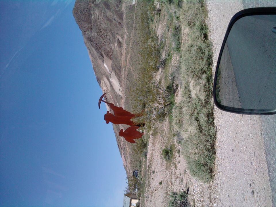 Desert landscape with a miner sculpture, seen from a vehicle's side mirror