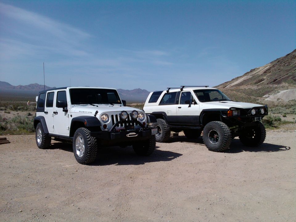 White Jeep Wrangler Rubicon and white Toyota 4Runner parked on dirt road in desert landscape