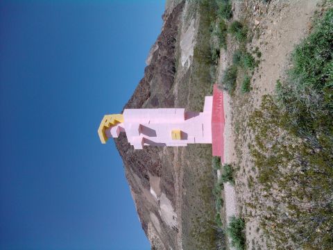 1985 Toyota 4Runner - A large, abstract pink and yellow sculpture stands on a barren hillside, with mountains in the background and a clear blue sky above.
