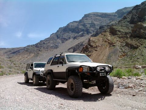 1985 Toyota 4Runner - A modified 1985 Toyota 4Runner leads a Jeep on a dusty trail through a mountainous desert landscape.