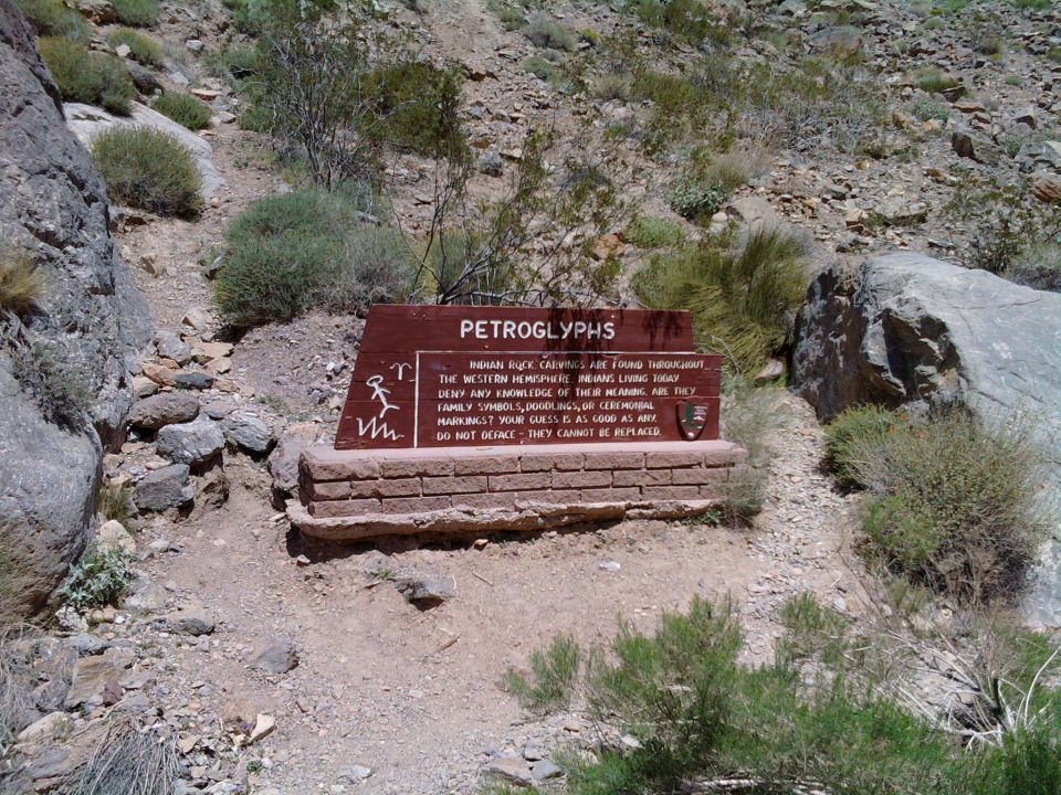 Petroglyph sign with text about Indian rock carvings, set in a rocky desert area