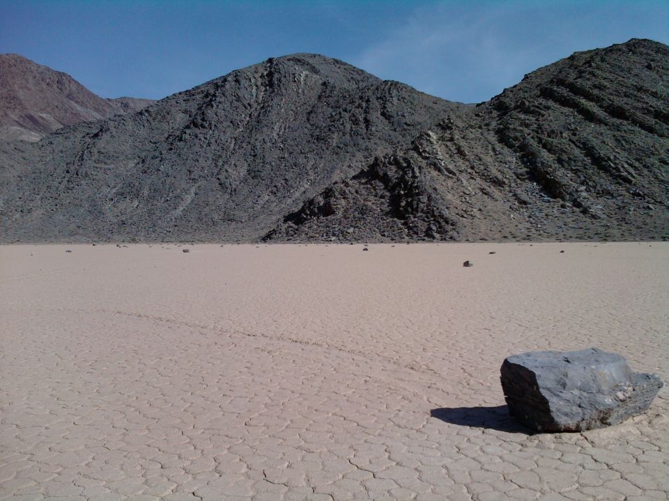 Dry lake bed with mountains in background and a rock in foreground. Supermotors logo at bottom right