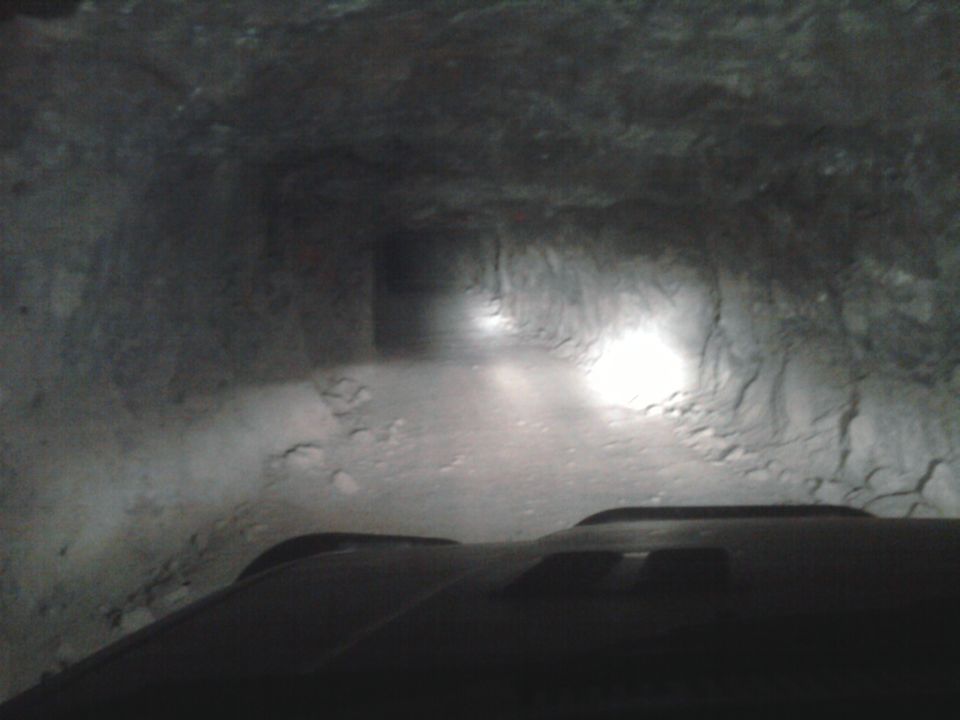 driving a vehicle into a dark, rocky tunnel with headlights on