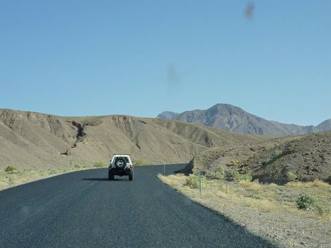 1985 Toyota 4Runner - A lone SUV travels down a desolate highway, surrounded by arid hills and distant mountains.