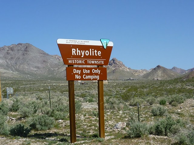 Brown sign for Rhyolite Historic Townsite with text 'Day Use Only. No Camping.' in a desert landscape