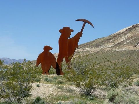 1985 Toyota 4Runner - A rustic metal sculpture depicting a prospector and a penguin stands in a dry, desert environment under a clear blue sky.