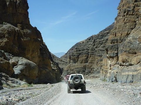 1985 Toyota 4Runner - Multiple SUVs, including a 1985 Toyota 4Runner, navigate a narrow dirt road through a desert canyon.
