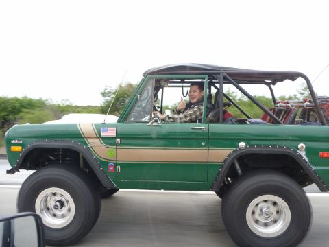 1985 Toyota 4Runner - A man drives a green Ford Bronco with a tan stripe and aftermarket modifications on a highway.