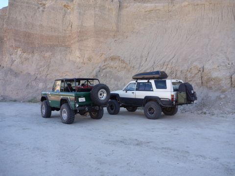 1985 Toyota 4Runner - Two modified SUVs are parked in a desert landscape with a large rock formation in the background.