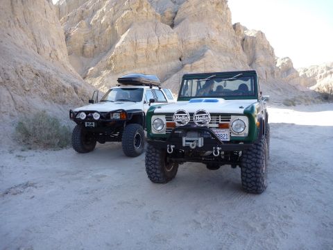 1985 Toyota 4Runner - Two modified off-road vehicles, a Ford Bronco and a Toyota 4Runner, are parked in a desert landscape.