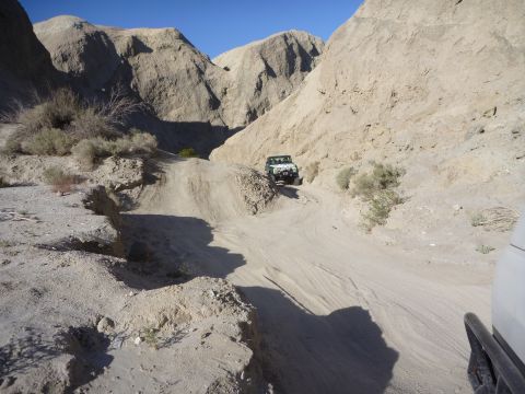 1985 Toyota 4Runner - A vehicle navigates a dusty trail through a narrow canyon under a clear blue sky.