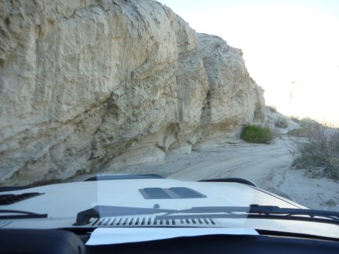 1985 Toyota 4Runner - View from inside a white SUV as it navigates a sandy track alongside a towering rock formation.