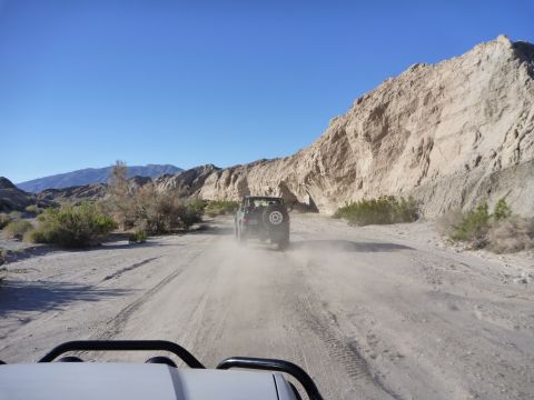 1985 Toyota 4Runner - Two SUVs traverse a dusty desert track under a clear blue sky.