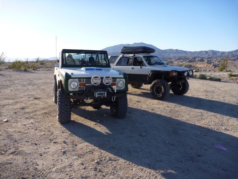 1985 Toyota 4Runner - Two modified SUVs are parked in a desert area under a clear blue sky.