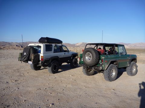 1985 Toyota 4Runner - Two modified SUVs, a green Ford Bronco and a white Toyota, are parked in a desert landscape.