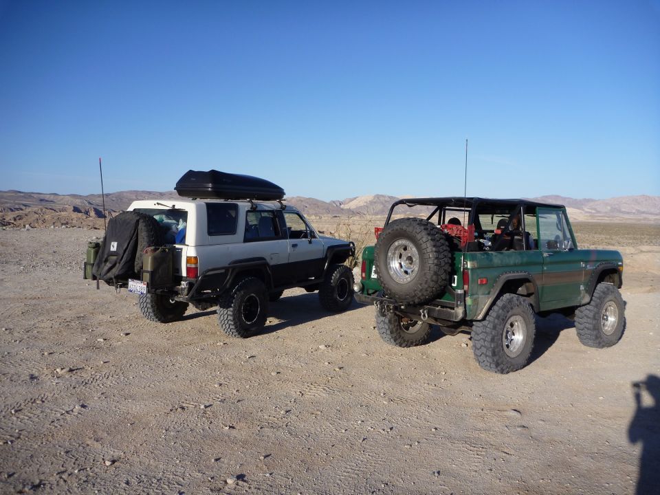 Green Ford Bronco with spare tire on back, parked next to a white Toyota SUV with a roof box
