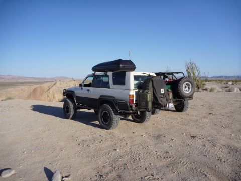 1985 Toyota 4Runner - Two off-road SUVs, including a 1985 Toyota 4Runner, are parked in a desert landscape under a clear blue sky.