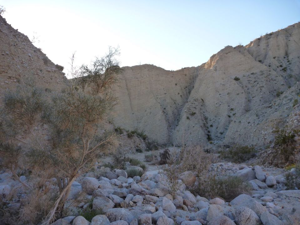 Desert canyon with rocky terrain and sparse vegetation under a clear sky. Supermotors logo visible