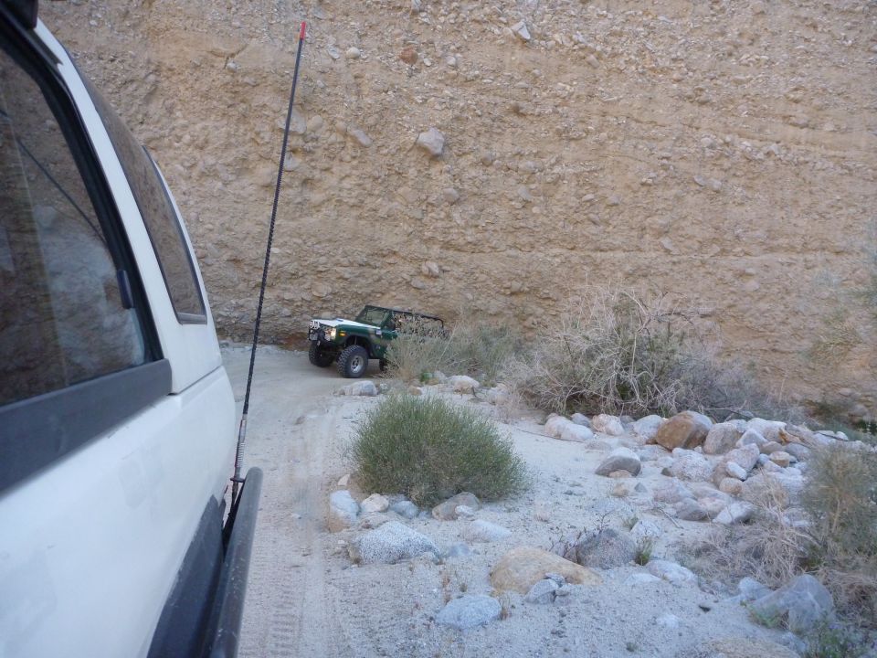 Green off-road vehicle with a white top and black roll cage parked on a dirt road