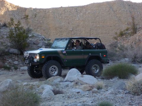 1985 Toyota 4Runner - A green 1976 Ford Bronco navigates a rocky desert trail with a roll cage visible.