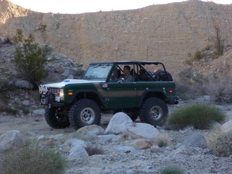 Green 1976 Ford Bronco off-roading in a rocky desert landscape