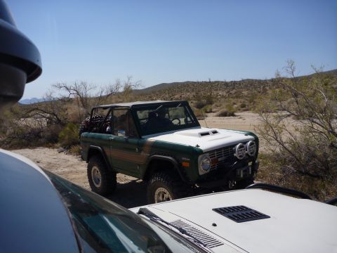 1985 Toyota 4Runner - Modified Ford Bronco with aftermarket hood scoop and driving lights sits in a desert environment.