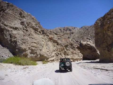 1985 Toyota 4Runner - A Jeep navigates a dry, rocky wash under a clear blue sky, surrounded by towering canyon walls.