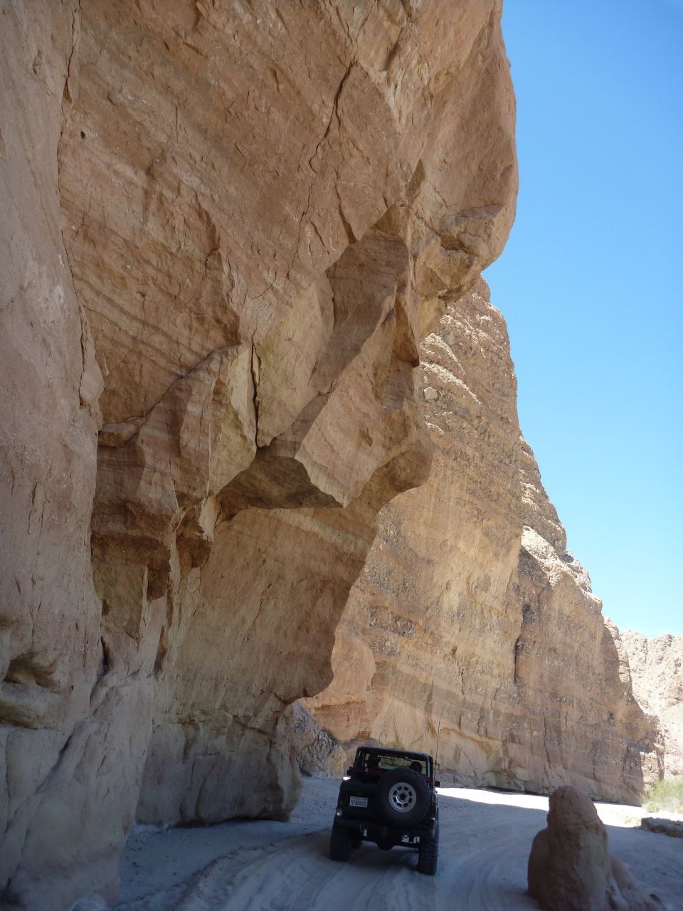 Dark green SUV driving on a dirt road through a canyon with large rock formations