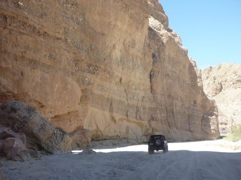 1985 Toyota 4Runner - A Jeep Wrangler navigates a dirt road through a narrow desert canyon under a clear blue sky.