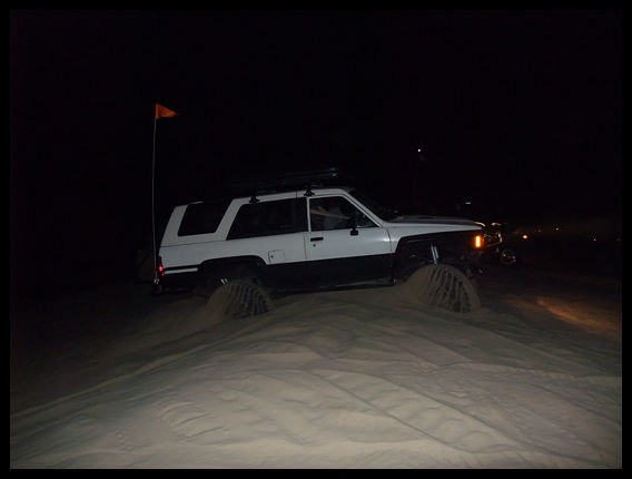 1985 Toyota 4Runner driving on sand dunes at night, with an orange flag on a pole