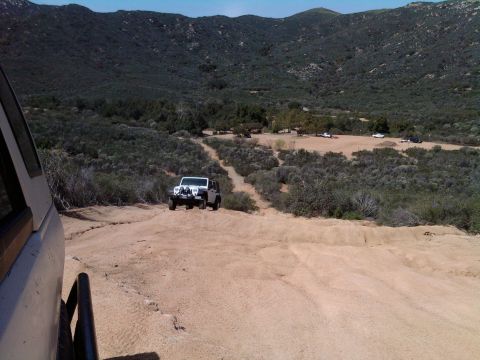 1985 Toyota 4Runner - A white Jeep navigates a dusty trail in a dry, mountainous area, with other vehicles visible in the distance.