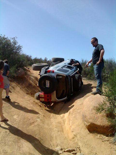 1985 Toyota 4Runner - An off-road SUV has rolled onto its side on a steep dirt trail, with onlookers assessing the situation.