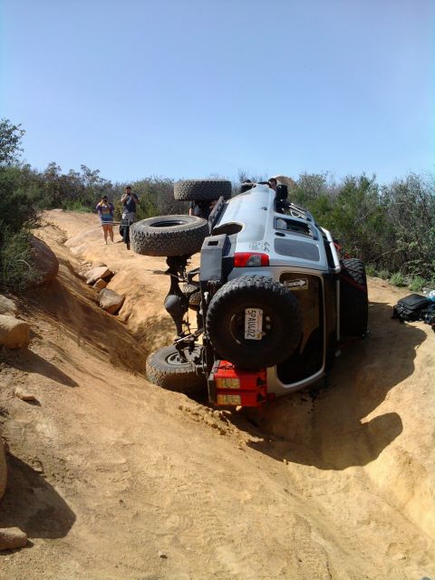 1985 Toyota 4Runner - A silver SUV has rolled onto its side while navigating a challenging dirt trail, with onlookers observing the scene.