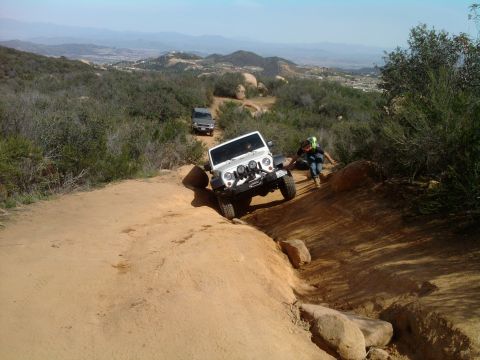 1985 Toyota 4Runner - Two off-road vehicles traverse a dusty mountain path under a clear sky.