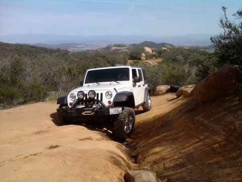 1985 Toyota 4Runner - A white Jeep Wrangler navigates a rocky dirt trail in a mountainous, arid landscape.