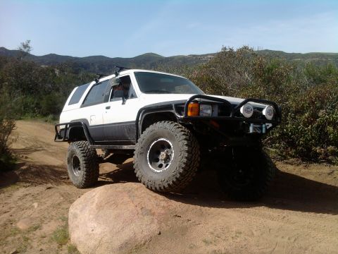 1985 Toyota 4Runner - Modified white Toyota 4Runner navigates a rocky off-road course under a clear sky.