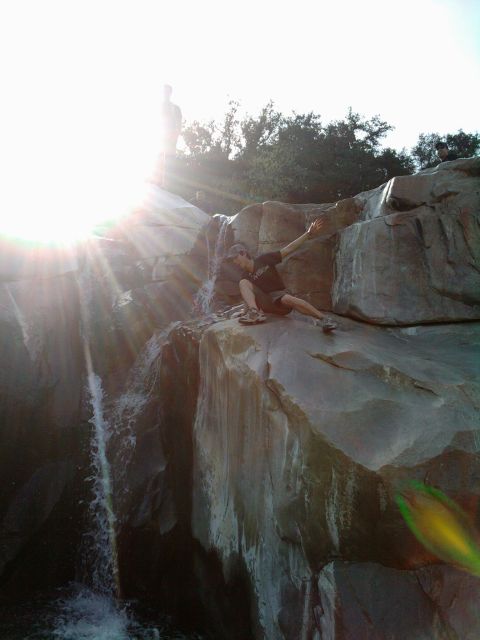 1985 Toyota 4Runner - Two people are visible near a waterfall, with the sun creating a strong lens flare effect.