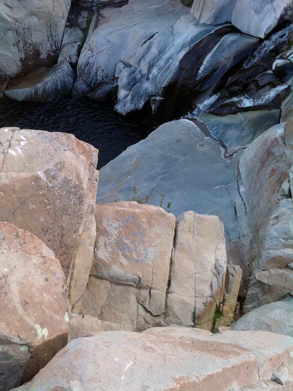 Rocky waterfall cascading into a dark pool, surrounded by large boulders