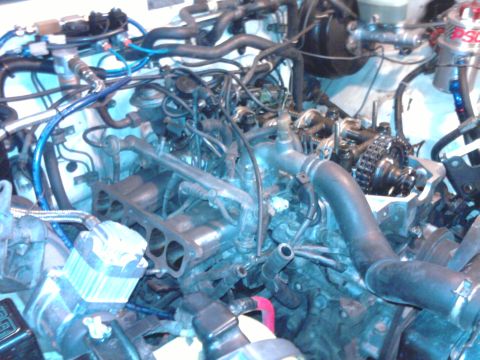1985 Toyota 4Runner - Close-up view of an engine bay, showing various mechanical parts and wiring. Text 'SUPERMOTORS' is visible.
