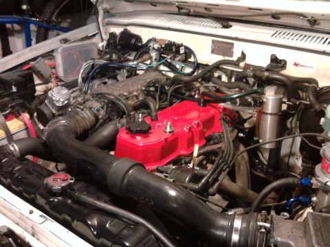 1985 Toyota 4Runner - Engine bay of a 1985 Toyota 4Runner, showing the engine with a red valve cover and various hoses and components.