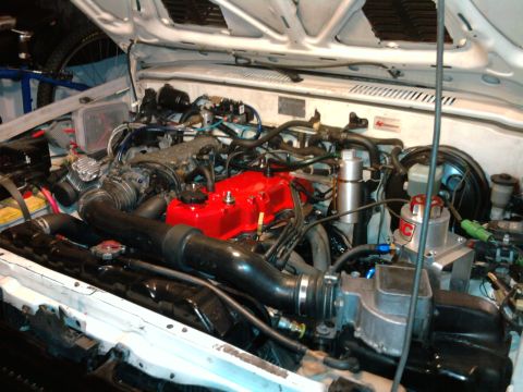 1985 Toyota 4Runner - The engine bay of a vehicle, a red-painted valve cover and black intake components.