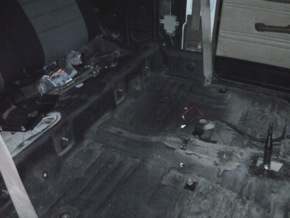 Interior of a stripped-down vehicle, showing bare floor and seats. Wires are visible