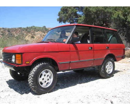 1990 Chevrolet Suburban - This red Range Rover is seen from a three-quarter front view on a dirt road, with a natural landscape behind it.