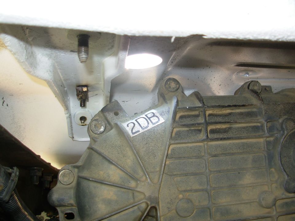 Underside view of aluminum transmission housing marked 2DB against white-painted frame.