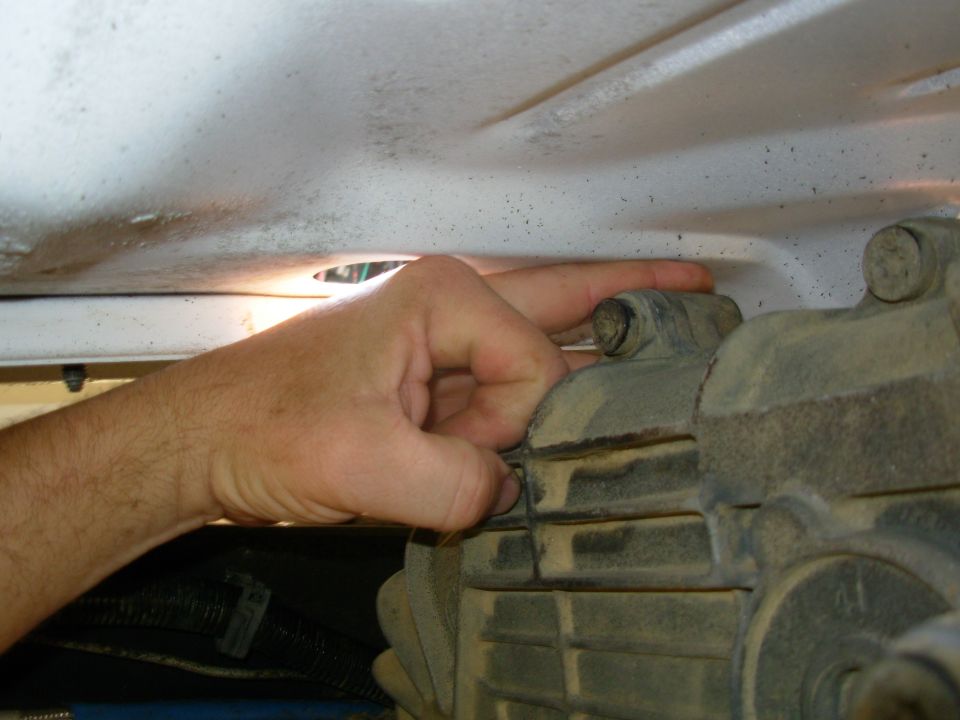 Hand on dusty aluminum transfer case housing under white truck underbody