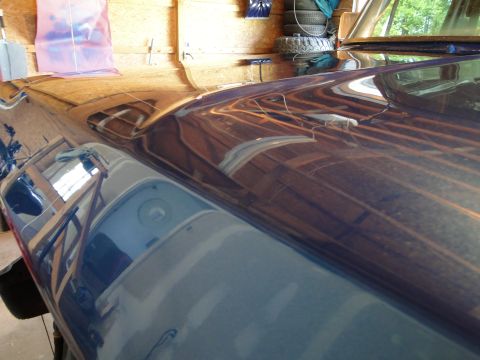 1978 Ford Bronco - The shiny hood of a dark blue vehicle reflects the wooden walls and ceiling of a garage.