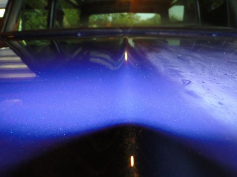 1978 Ford Bronco - Close-up view of a blue metallic car hood with a prominent central crease and visible reflections.