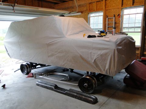1978 Ford Bronco - A vehicle is covered by a tarp, revealing its shape and some of its undercarriage and wheels.